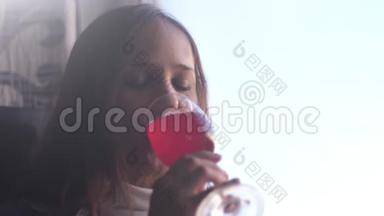 孤独的漂亮女孩正在喝红酒，坐在窗边。 慢动作。 3840x2160